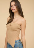 Woman wearing a beige strapless top and blue jeans with a beige background