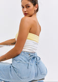 Woman wearing a yellow and white strapless top with blue jeans on a light gray background
