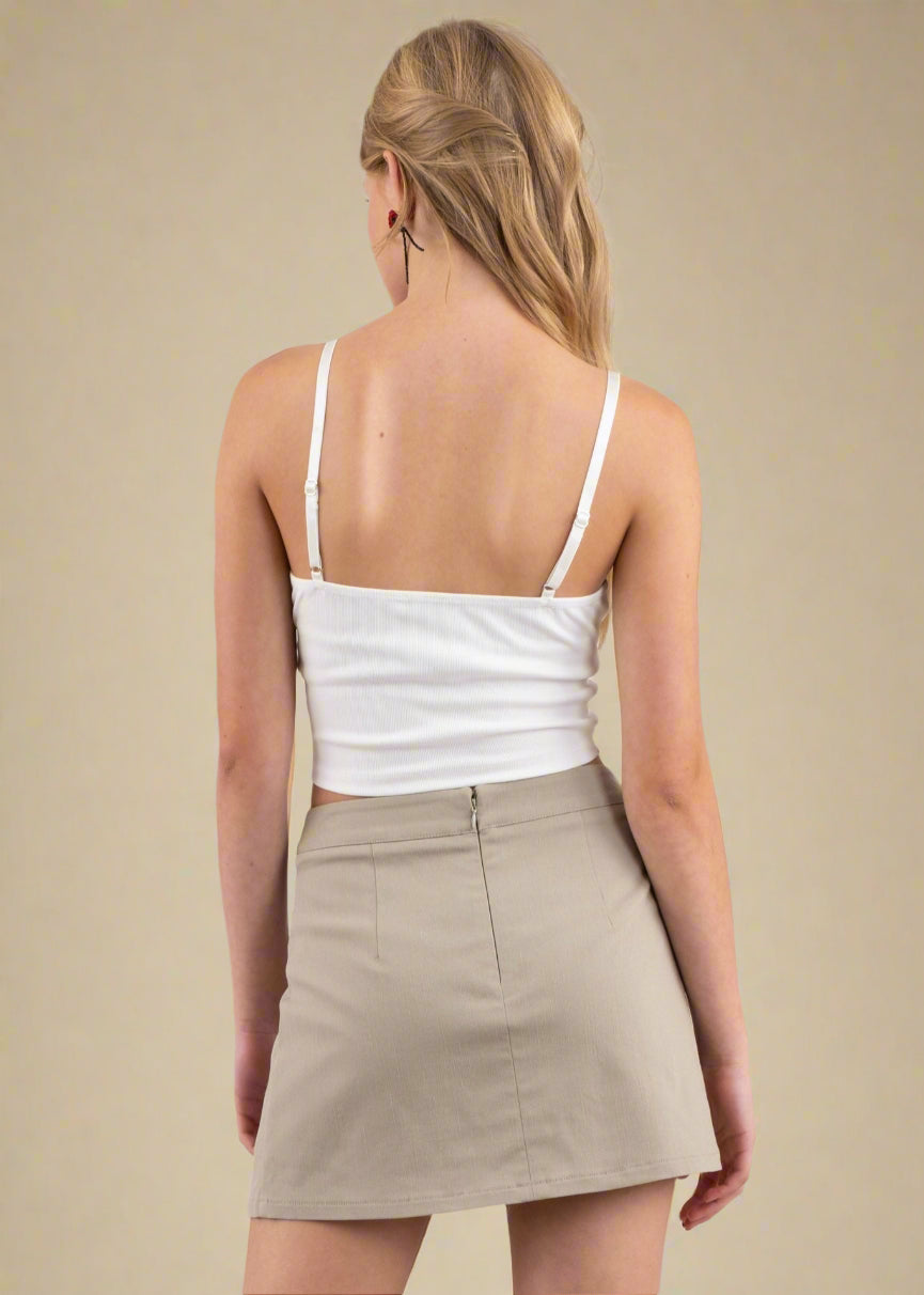Woman wearing a white tank top and beige skirt on a plain background