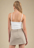 Woman wearing a white tank top and beige skirt on a plain background