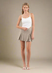 Woman wearing a white tank top and beige skirt on a plain background