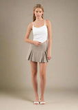 Woman wearing a white tank top and beige skirt on a plain background
