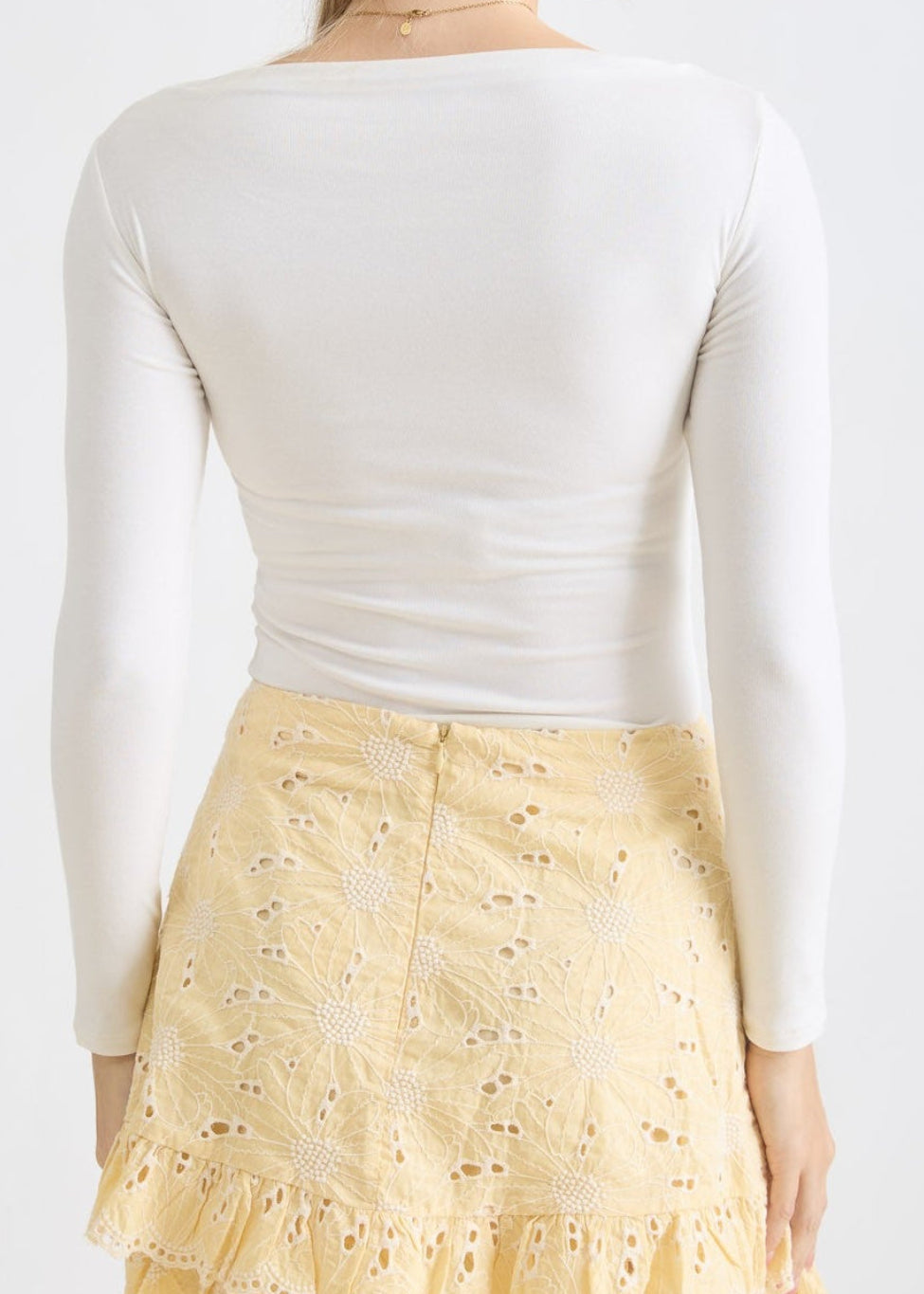 Woman wearing a white long-sleeve top and a yellow lace skirt on a plain background