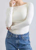 Woman wearing a white long-sleeve top and blue jeans against a plain background