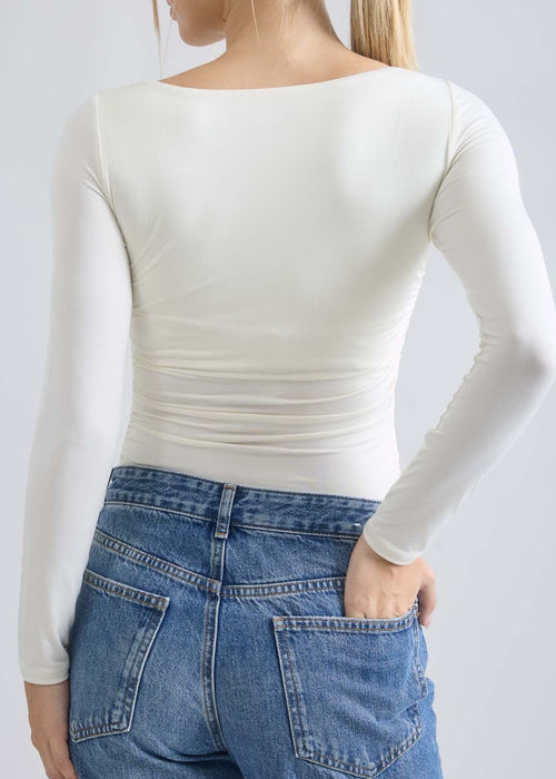 Person wearing a white long-sleeve top and blue jeans on a plain background