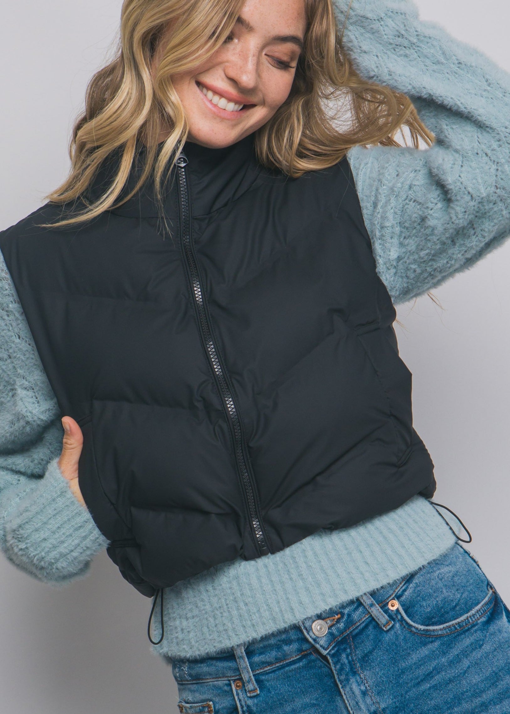 Woman wearing a black puffer vest over a light blue sweater with a plain background