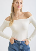 Woman wearing a white off-shoulder top and blue jeans on a white background