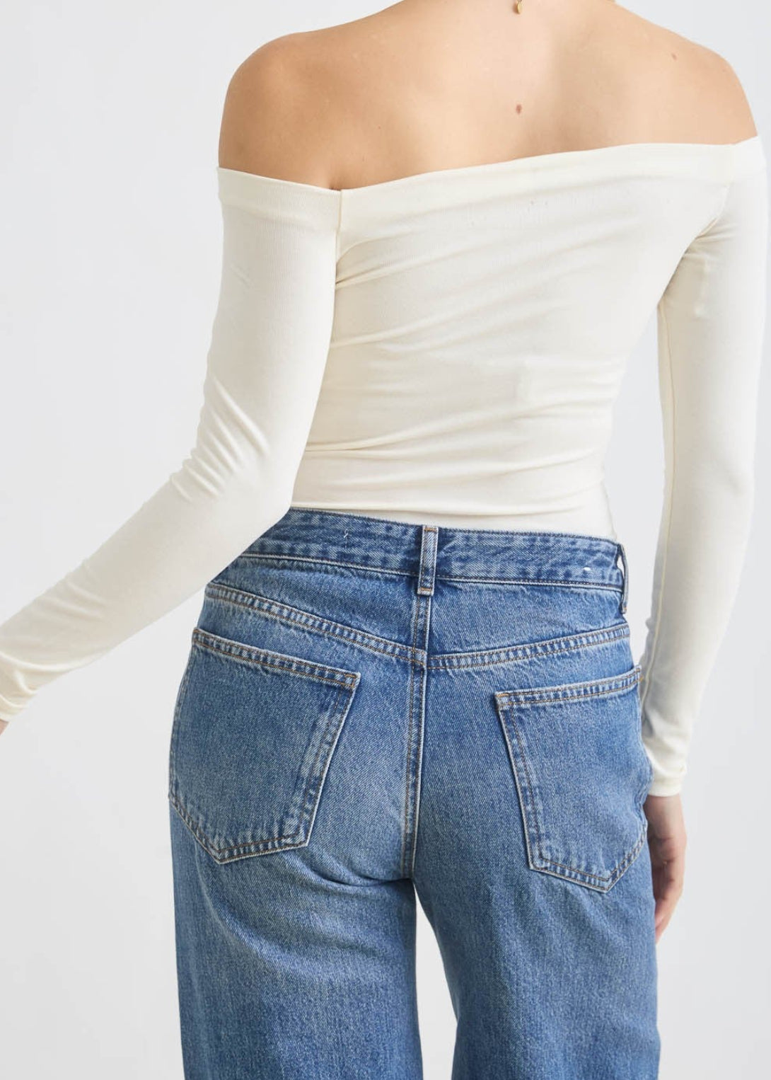 Woman wearing a white off-shoulder top and blue jeans on a plain background