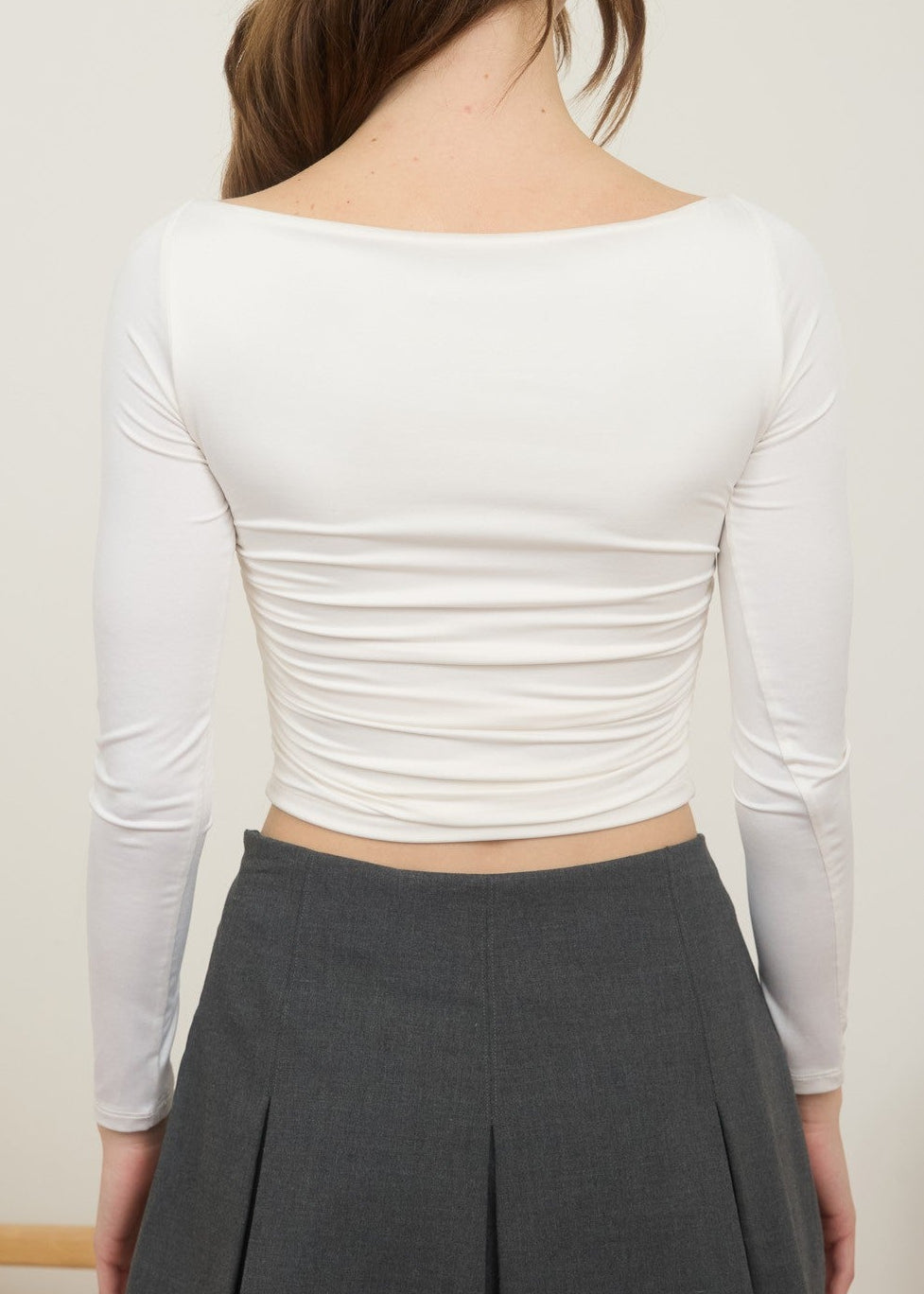 Person wearing a white long-sleeve top and gray pleated skirt against a plain background