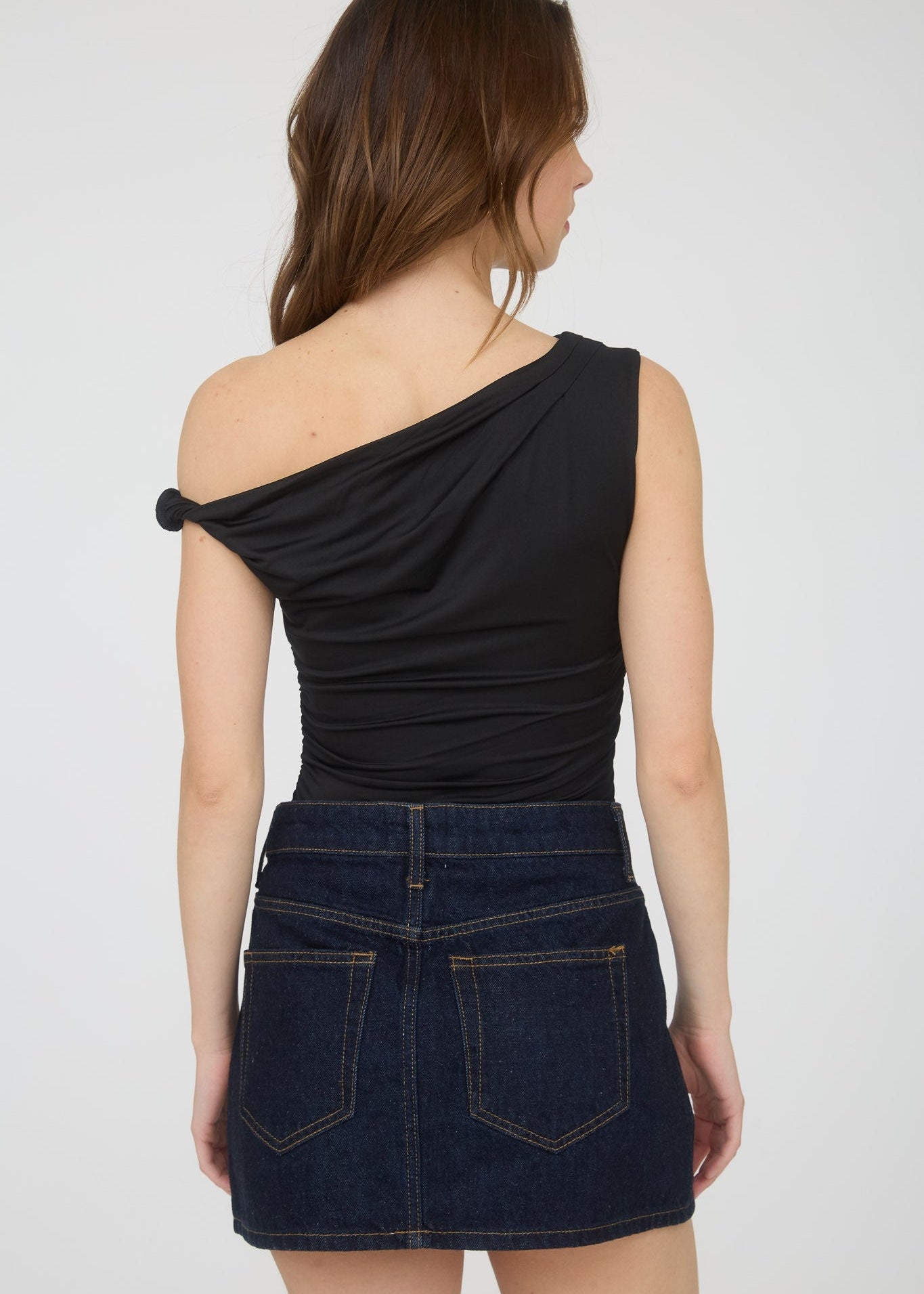 Woman wearing a black one-shoulder top and denim skirt on a white background
