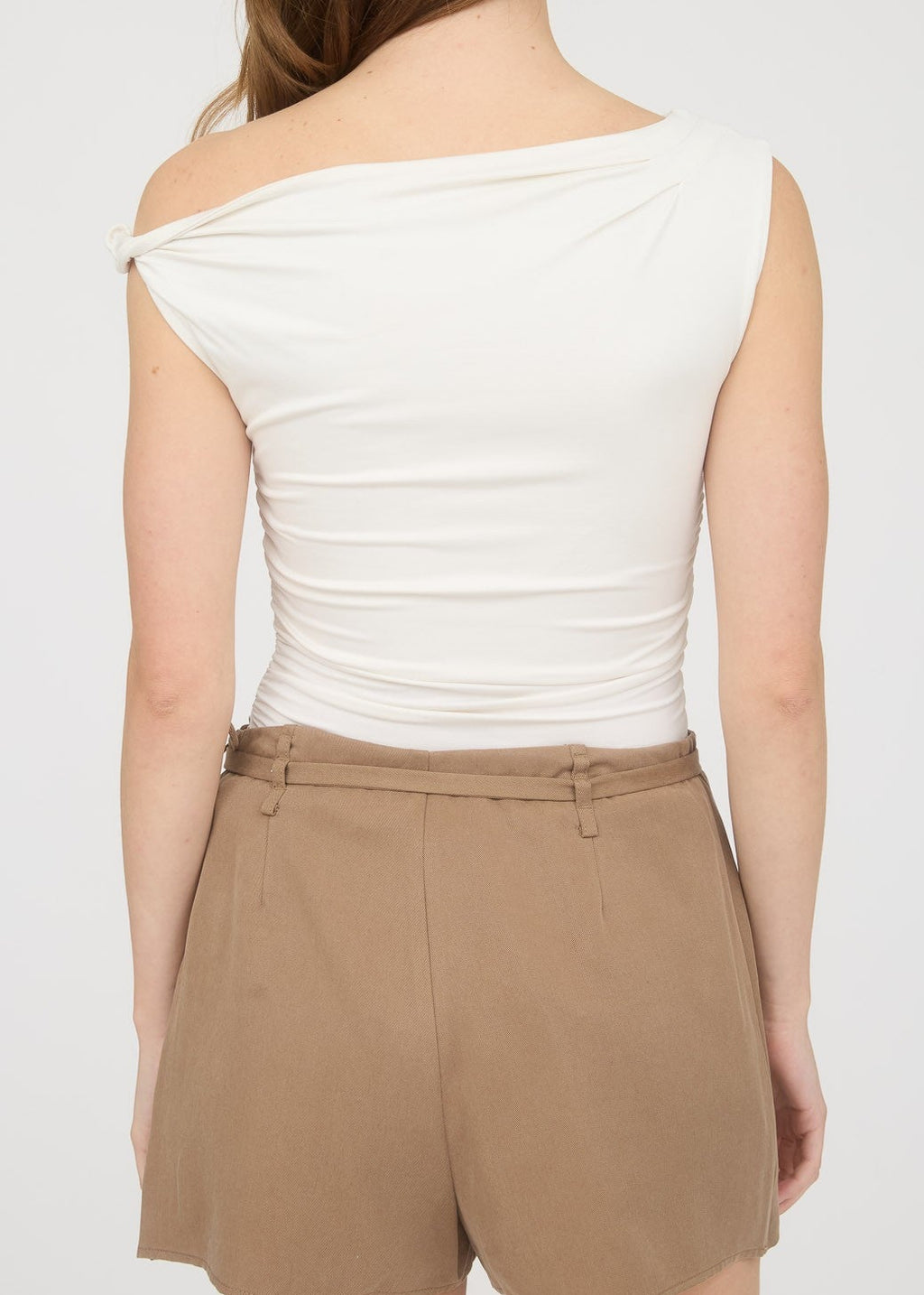 Woman wearing a white sleeveless top and beige shorts on a plain background