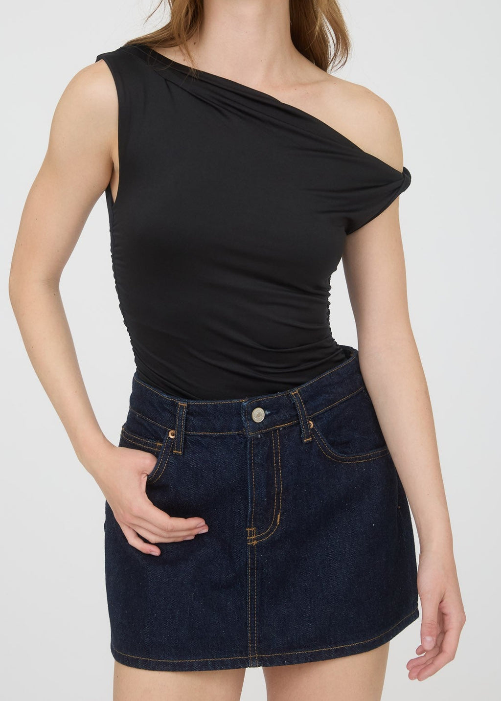 Woman wearing a black one-shoulder top and dark denim skirt on a white background