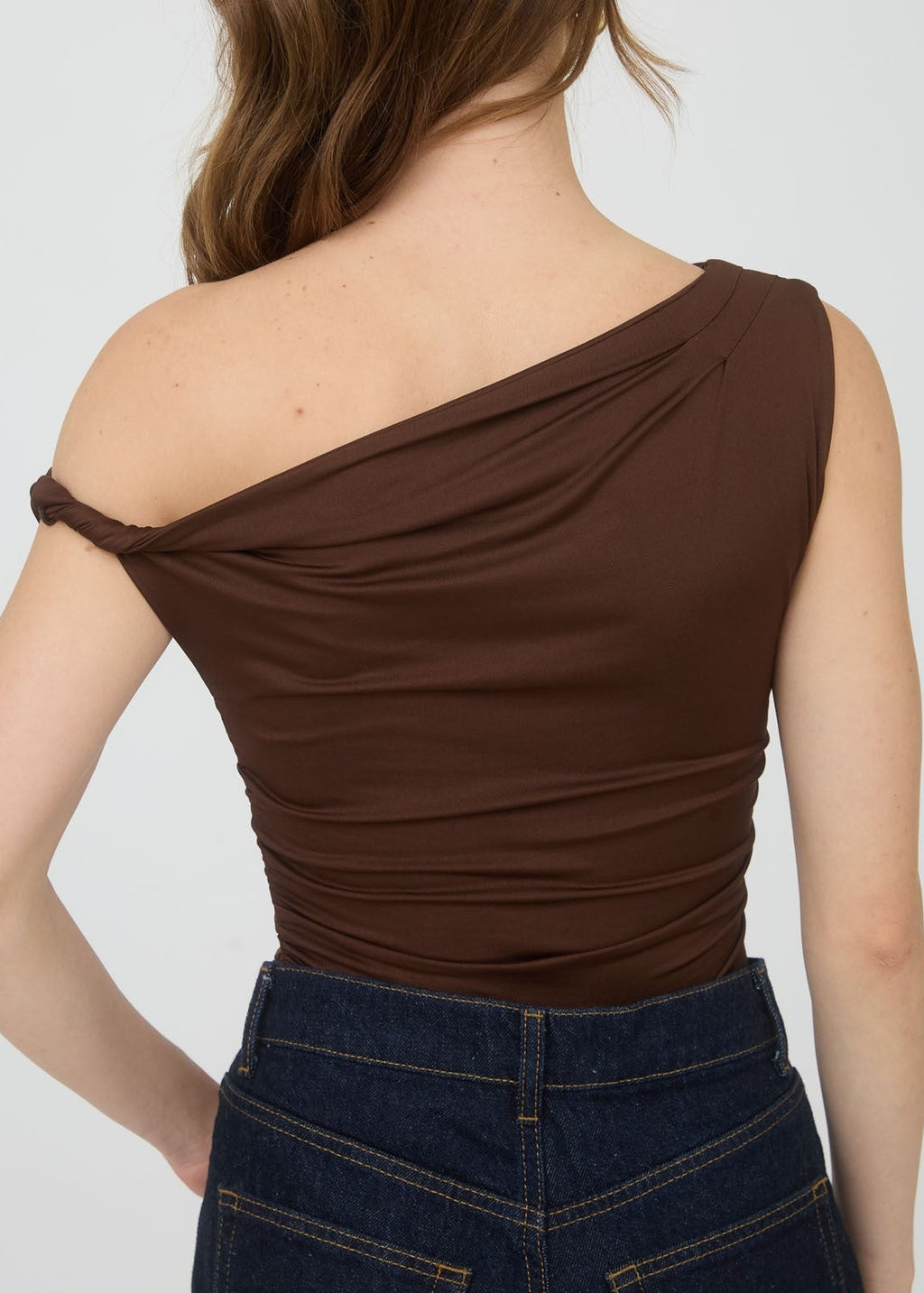 Woman wearing a brown one-shoulder top against a white background