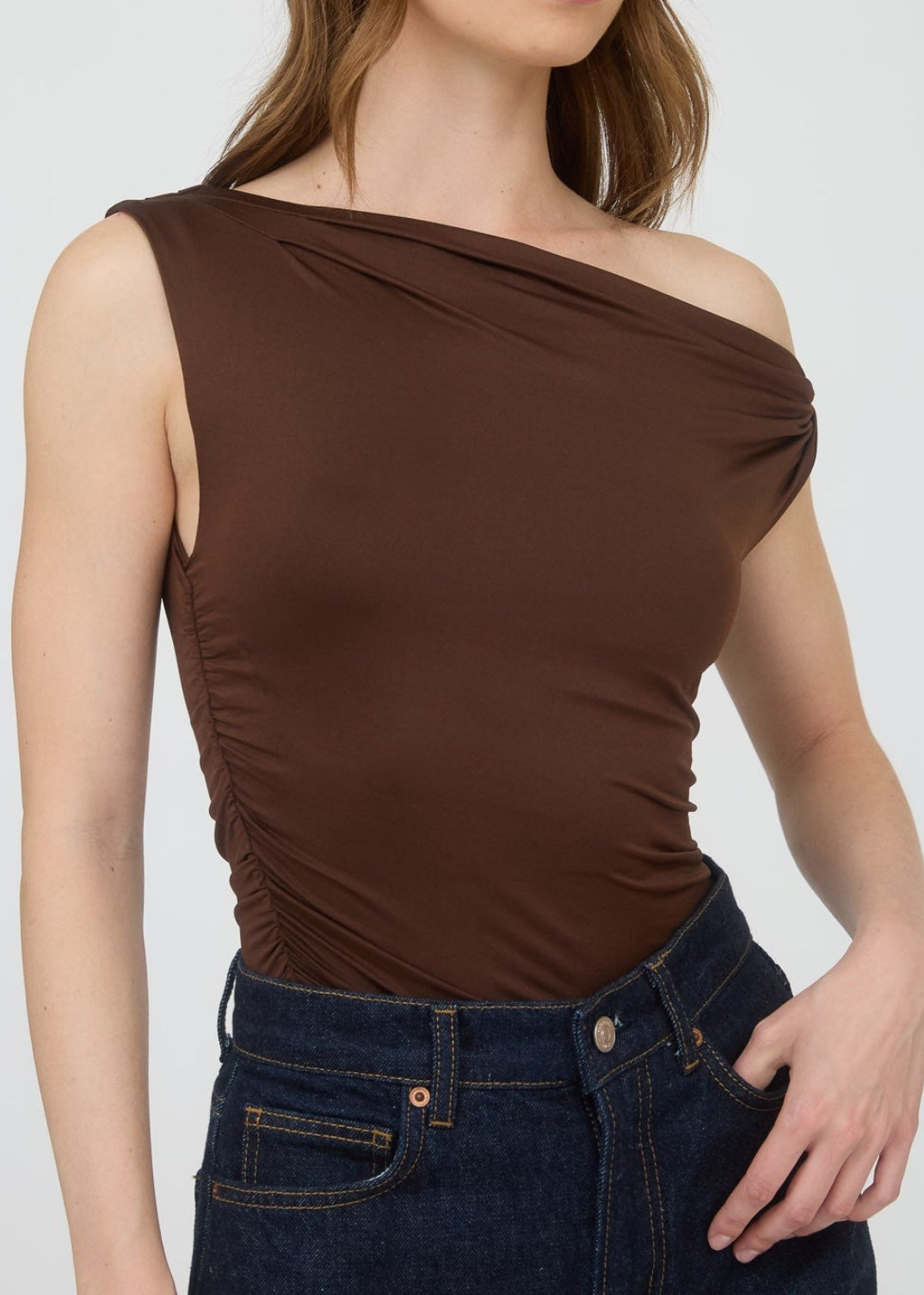 Woman wearing a brown one-shoulder top and blue jeans on a white background