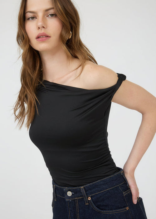 Woman wearing a black one-shoulder top and blue jeans on a white background