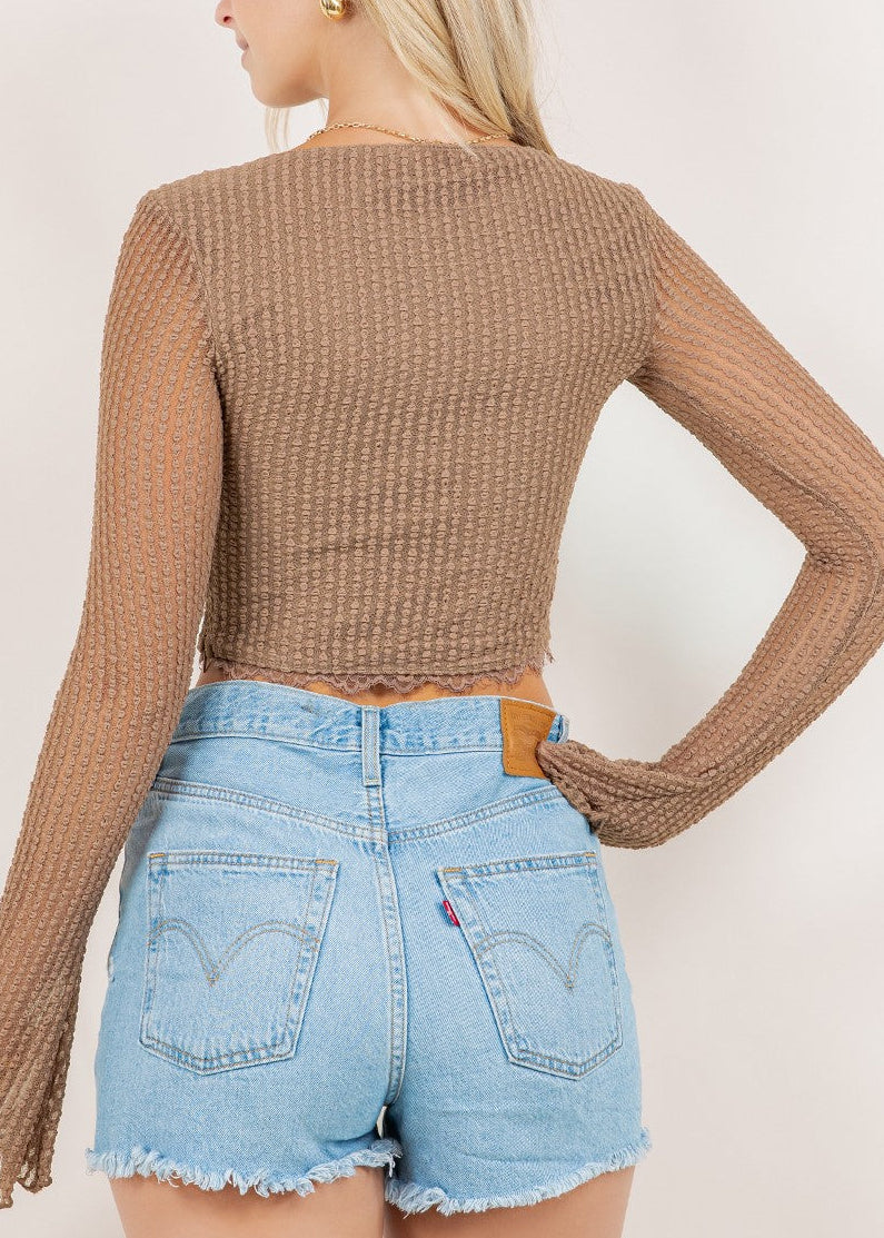 Woman wearing a brown long-sleeve top and light blue denim shorts against a white background