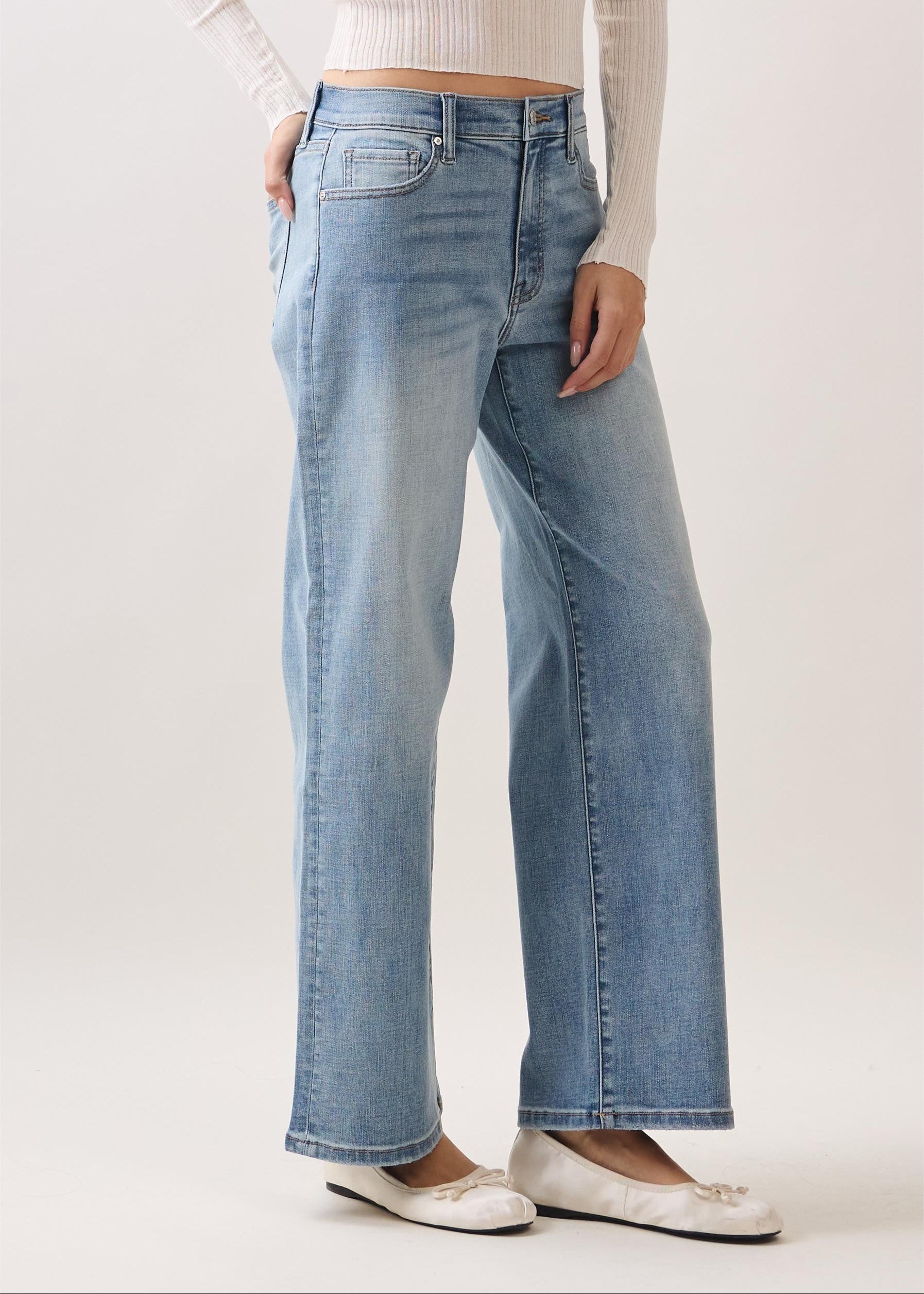 Person wearing light blue jeans and a white top on a plain background