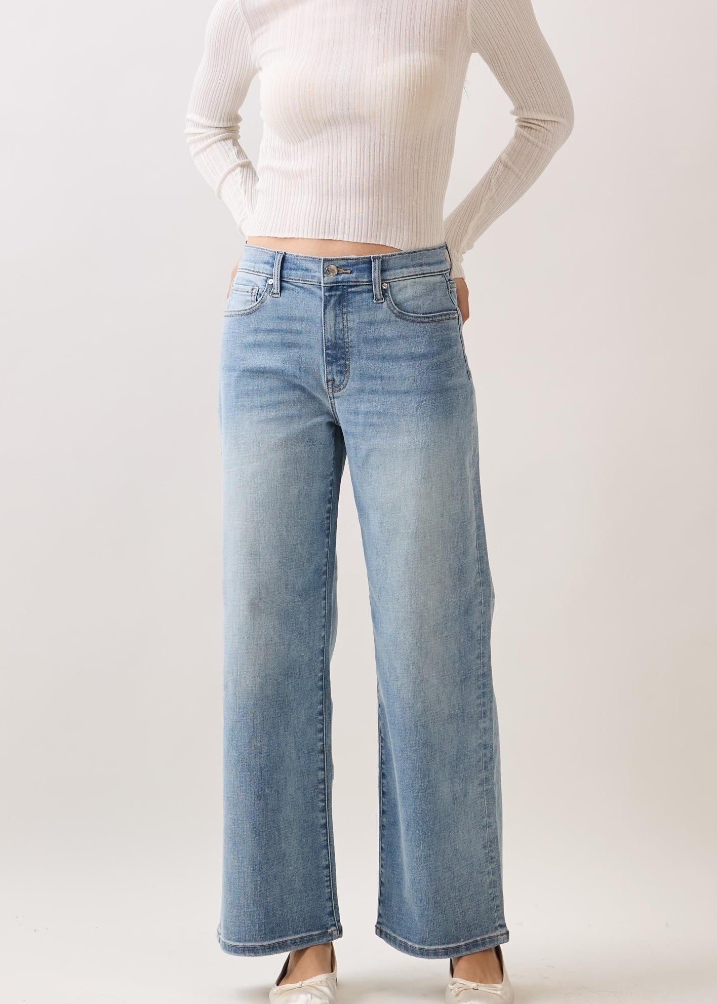 Woman wearing a white long-sleeve top and light blue jeans on a plain background