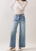 Woman wearing a white long-sleeve top and light blue jeans against a plain background