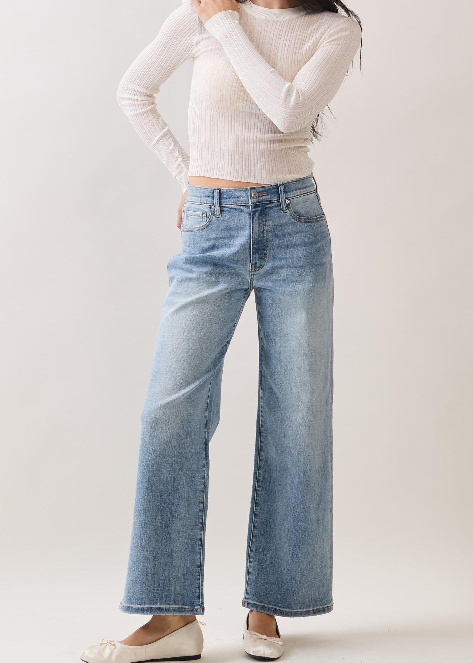Woman wearing a white long-sleeve top and light blue jeans against a plain background